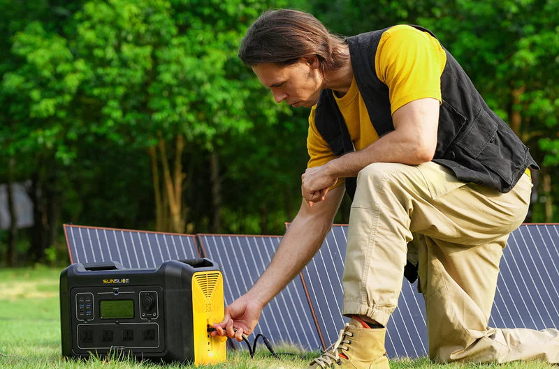 Homme utilisant une station d'énergie solaire portable connectée à des panneaux photovoltaïques en extérieur