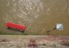 Photographie d'une inondation avec un banc rouge et un lampadaire sous l'eau