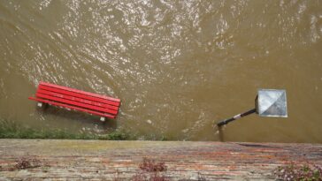 Photographie d'une inondation avec un banc rouge et un lampadaire sous l'eau
