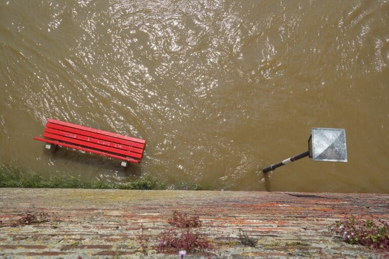 Photographie d'une inondation avec un banc rouge et un lampadaire sous l'eau