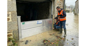 Deux techniciens en gilet orange contrôlent un batardeau aluminium installé devant un garage pendant une inondation de rue