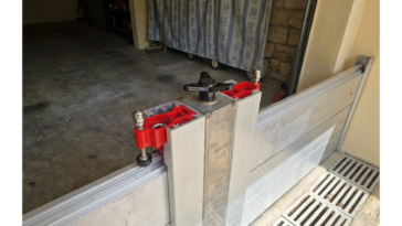 Gros plan sur un batardeau amovible en aluminium avec système de serrage rouge et molette noire installé devant l’entrée d’un garage
