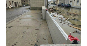 Batardeau amovible en aluminium retenant l’eau boueuse et les débris dans une rue inondée tandis que le trottoir derrière la barrière reste sec