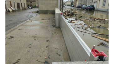 Batardeau amovible en aluminium retenant l’eau boueuse et les débris dans une rue inondée tandis que le trottoir derrière la barrière reste sec