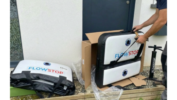 Homme préparant un batardeau gonflable Flowstop encore plié devant une porte d’entrée, avec sac de transport et pompe à pied à proximité
