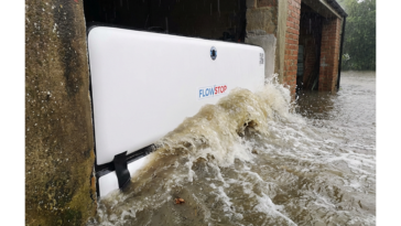 Batardeau gonflable Flowstop plaqué dans l’ouverture d’un garage, retenant une vague d’eau boueuse lors d’une inondation