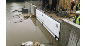 Batardeau gonflable Flowstop fixé contre un mur de béton retenant l’eau de crue autour d’un chantier, avec des ouvriers en gilet jaune observant la montée des eaux