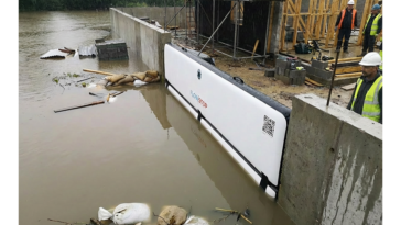 Batardeau gonflable Flowstop fixé contre un mur de béton retenant l’eau de crue autour d’un chantier, avec des ouvriers en gilet jaune observant la montée des eaux