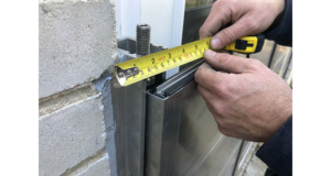 Mains d’un technicien mesurant au mètre ruban un montant en aluminium pour installer un batardeau de porte anti inondation étanche