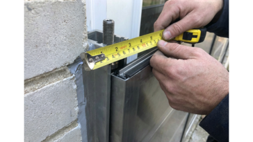 Mains d’un technicien mesurant au mètre ruban un montant en aluminium pour installer un batardeau de porte anti inondation étanche