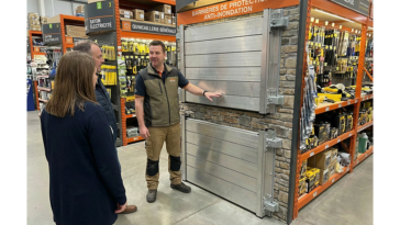 Vendeur en magasin de bricolage expliquant à deux clients les différents modèles de batardeaux en aluminium exposés au rayon barrières de protection anti inondation