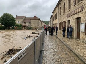 Batardeau StopFlood protégeant une rue et des bâtiments publics contre une crue de rivière chargée de débris.