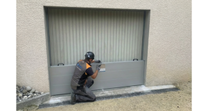 Technicien agenouillé installant un batardeau en aluminium devant une porte de garage pour protéger le bâtiment des inondations