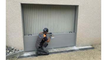 Technicien agenouillé installant un batardeau en aluminium devant une porte de garage pour protéger le bâtiment des inondations